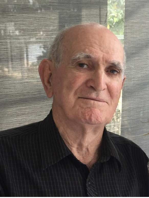 Noel Greenaway, an elderly bald man in a dark pinstriped shirt, photographed indoors against a woven blind.