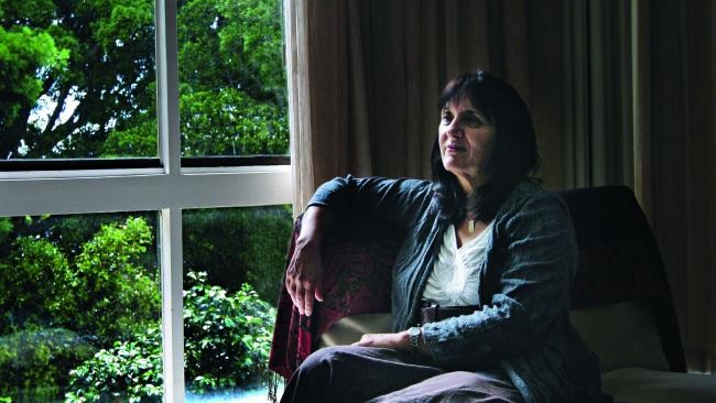 Cathy Kezelman seated in an armchair beside a large window, looking out over a green garden.