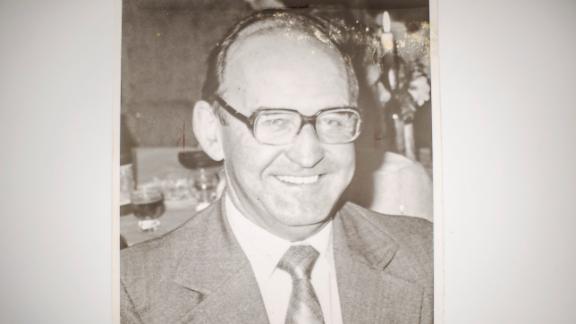 A black-and-white photograph of Arthur Easton, a smiling middle-aged man in glasses, a suit and a patterned tie, seated at a table at a social gathering.