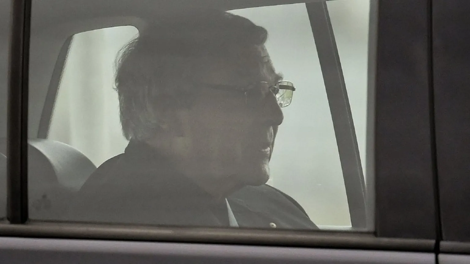Cardinal George Pell seen in profile through the window of a car, wearing glasses and dark clerical dress, as he is driven away from Victoria's Barwon Prison after his convictions were overturned.
