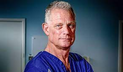 Portrait of Dr Richard Shepherd in blue surgical scrubs, arms folded, looking at the camera.
