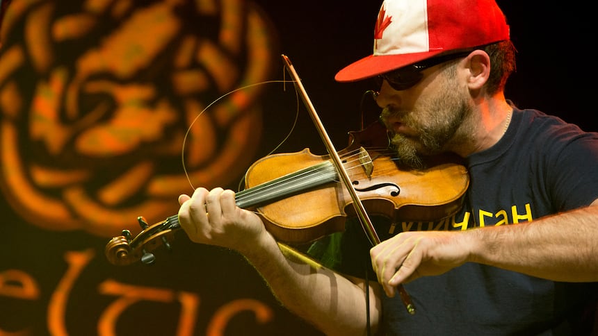 A man plays the fiddle while wearing a baseball hat in the colours of the Canadian flag.