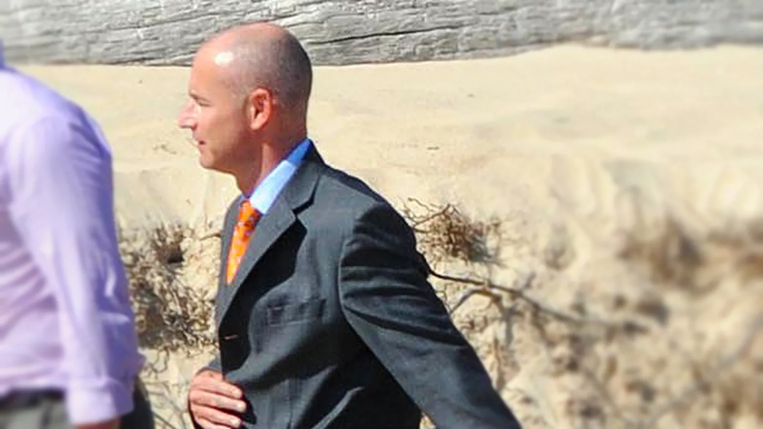 Neil Hibberd, in a suit and open-necked shirt, standing outdoors in Kenya.