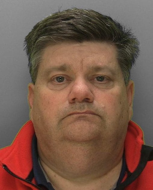 Police handout mugshot of Carl Beech, in a red jacket against a grey background.