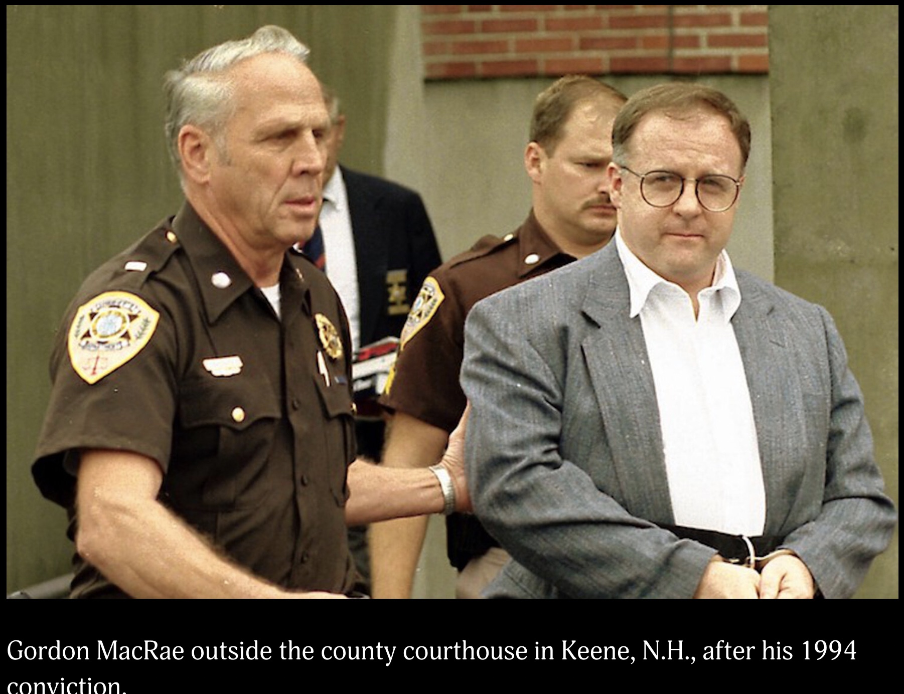 Gordon MacRae, in a grey jacket and handcuffs, escorted from the county courthouse in Keene, New Hampshire by two uniformed sheriff’s deputies after his 1994 conviction.