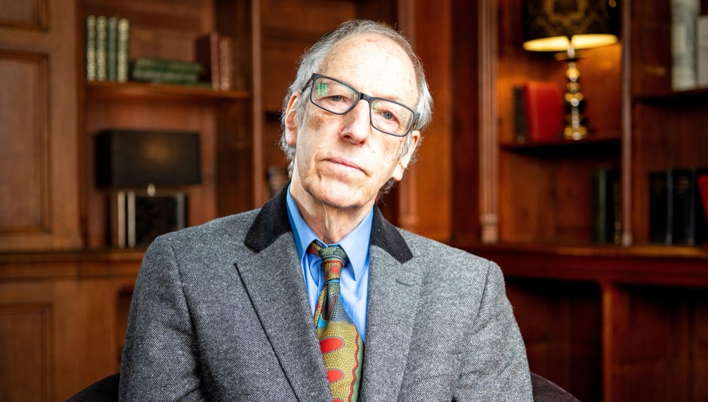 Professor David Canter, in a grey tweed jacket, blue shirt and patterned tie, sits in a wood-panelled room lined with bookshelves.