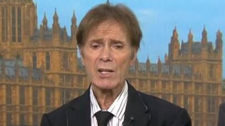 Sir Cliff Richard speaking, seated, in a dark jacket and open-necked shirt.